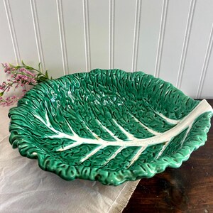 May include: A green ceramic serving dish shaped like a large leaf. The dish has a textured surface with white veins and a scalloped edge. The leaf-shaped dish is a decorative piece.