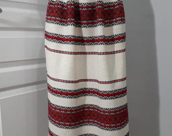 May include: A cream-colored midi skirt featuring horizontal bands of intricate red and black geometric embroidery. The skirt has a high waist with subtle pleats at the waistband and a straight silhouette that ends in a fringed hemline.