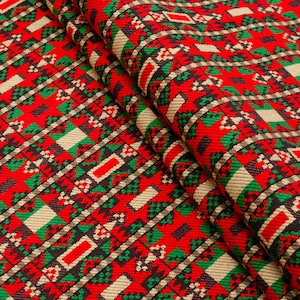 Puede incluir: Tela roja, verde y beige con un patrón geométrico. La tela está doblada por la mitad, mostrando el patrón en ambos lados.