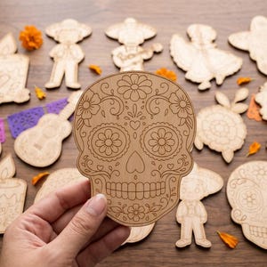 May include: A light-colored wooden cutout in the shape of a sugar skull, featuring intricate laser-engraved floral and scroll patterns. The skull is surrounded by various other wooden cutouts including figures, flowers, and a guitar.