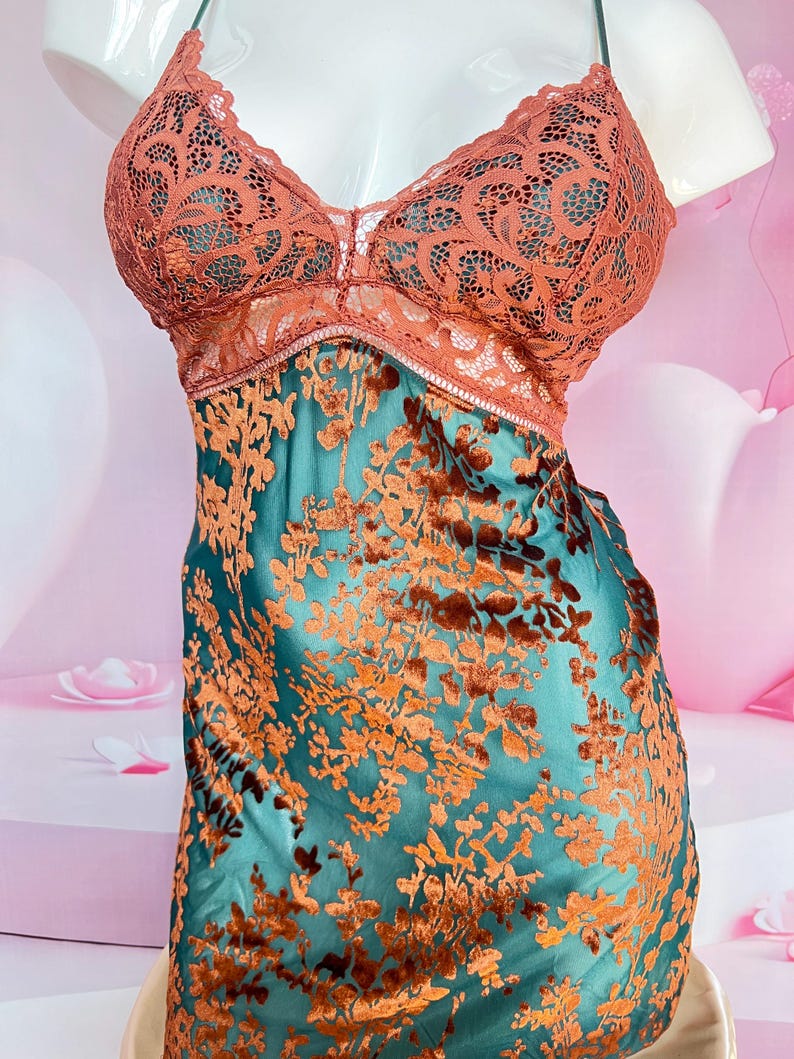 May include: A teal slip dress with a floral pattern in shades of orange and brown. The bodice features a lace overlay in a coral color. The dress has thin straps and a V-neckline.