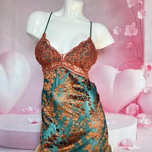 May include: A teal and copper-colored lingerie piece displayed on a mannequin. The top features a copper-colored lace design, while the lower portion has a floral pattern. The garment is supported by thin, dark straps.