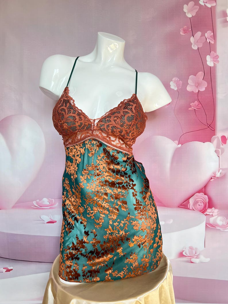 May include: A teal and copper-colored lingerie piece displayed on a mannequin. The top features a copper-colored lace design, while the lower portion has a floral pattern. The garment is supported by thin, dark straps.