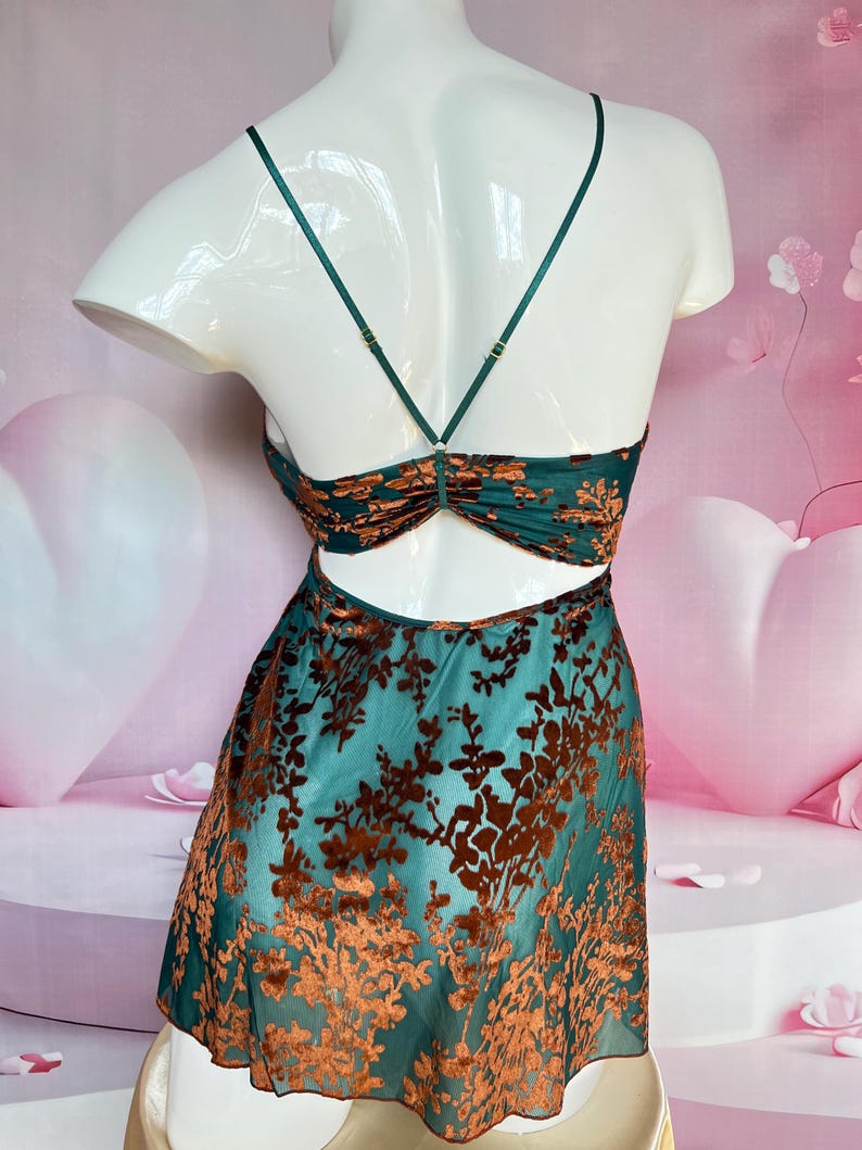 May include: A teal-colored slip dress with a floral pattern in a darker shade of brown. The dress features thin straps and a low back. The floral pattern is a velvet-like material. The dress is displayed on a white mannequin.