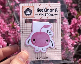 May include: A bookmark for books featuring a pink cherry character with a smiling face. The bookmark is on a grid-patterned background with the words "Bookmark - FOR BOOKS" and the word "cataqi collent".