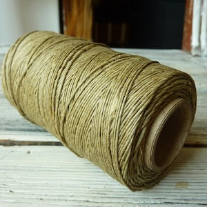 May include: A spool of natural green twine, wound tightly and ready for use. The twine is made of natural fibers and has a rustic look.