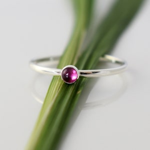 May include: A simple silver ring with a small, round, cabochon-cut, pink gemstone.