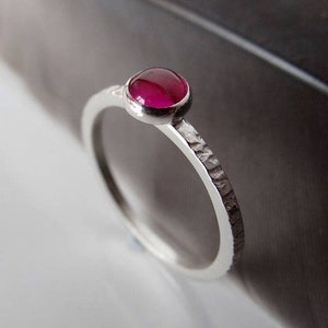 May include: A silver ring with a textured band and a single, round, pink gemstone.