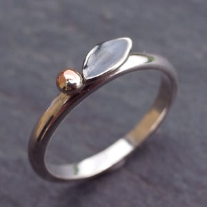 May include: A silver ring with a leaf design and a small gold bead. The leaf is flat and has a smooth, polished surface.
