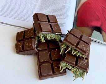 May include: A stack of chocolate bars with a green filling. The chocolate is dark brown and the filling is a light green. The bars are broken and stacked on top of each other.