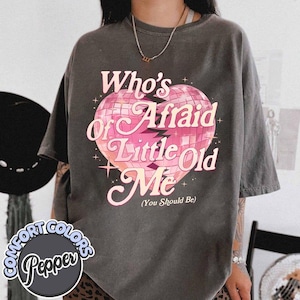May include: A gray t-shirt with a pink and white graphic of a broken heart with the text "Who's Afraid of Little Old Me (You Should Be)"