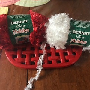 May include: Two spools of Bernat Boa Holidays yarn, one red and one white, each with a label that reads "100 g/3.5 oz Bernat Boa Holidays".