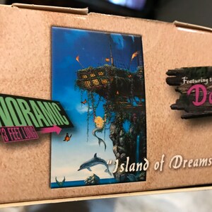 May include: A 500 piece panoramic jigsaw puzzle featuring the art of David. The puzzle depicts a whimsical island with a treehouse, a mermaid, and a dolphin. The box is brown with a pink and green "Panoramic 3 feet long" label.