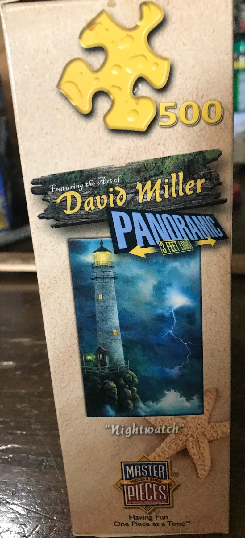 May include: A 500-piece jigsaw puzzle featuring a lighthouse with a stormy sky and lightning. The puzzle box is labeled "Panoramic 3 Feet Long" and "Nightwatch" by artist David Miller. The box also features the Master Pieces logo.