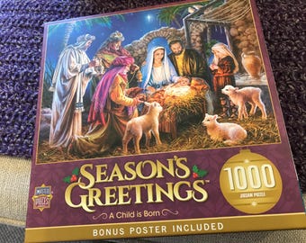 Puede incluir: Un rompecabezas de 1000 piezas con temática navideña. La caja del rompecabezas presenta una pintura de la escena de la Natividad con el texto "Season's Greetings" y "A Child is Born". Incluye un póster de bonificación.