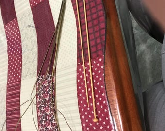May include: A close-up of knitting needles and circular needles on a patterned surface. The needles are made of wood and metal. The surface has a patchwork design with red, white, and burgundy colors.