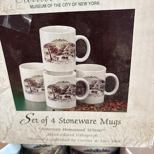 May include: Set of four stoneware mugs featuring a winter scene with a house, trees, and a horse-drawn carriage. The mugs are white with a handle and a detailed illustration. The text "Currier & Ives" and "American Homestead Winter" are visible.