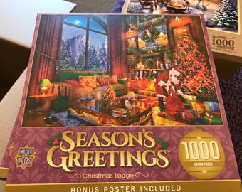 Könnte beinhalten: Ein 1000-teiliges Puzzle mit dem Titel "Season's Greetings Christmas Lodge". Die Puzzlebox zeigt eine gemütliche Weihnachtsszene mit einem geschmückten Baum, einem Kamin und dem Weihnachtsmann. Das Bild enthält einen Blick auf eine verschneite Berglandschaft.
