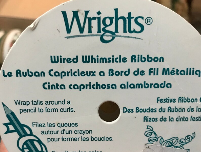 May include: A spool of Wrights Wired Whimsicle Ribbon. The label is white with teal text that reads "Wired Whimsicle Ribbon" and instructions for curling the ribbon. The ribbon is designed for festive occasions.