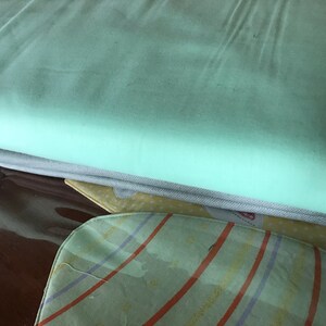 May include: A stack of folded fabric in shades of mint green, gray, and yellow. The top layer is a smooth, solid mint green. Below it is a gray fabric, and a patterned yellow and red fabric is visible at the bottom.