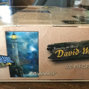 May include: A 500-piece jigsaw puzzle featuring the art of David Miller. The puzzle depicts a lighthouse with a stormy sky and lightning in the background. The title of the artwork is "Nightwatch".