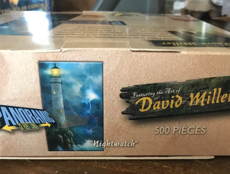 May include: A 500-piece jigsaw puzzle featuring the art of David Miller. The puzzle depicts a lighthouse with a stormy sky and lightning in the background. The title of the artwork is "Nightwatch".