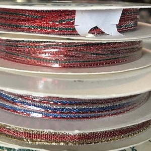 May include: Spools of decorative ribbon in various colors, including red, blue, and gold. The ribbon is metallic and has a woven texture. The spools are stacked on top of each other, creating a visually appealing display. Perfect for crafting and gift wrapping.