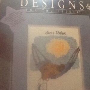 May include: A cross-stitch pattern featuring a person relaxing in a hammock with the text "Just Relax" above them. The pattern is on a white background with blue and yellow accents.