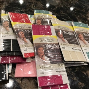 May include: Assortment of 10 rolls of Wright's Soft and Easy Hem Tape in various colors, including red, pink, burgundy, white, and blue. Each roll is 3 yards long and 1/2 inch wide. The packaging features a woman's face and the text "Soft and Easy Hem Tape" and "Wrights".
