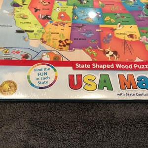 Puede incluir: Un rompecabezas de madera de mapa de EE. UU. colorido con capitales estatales. Las piezas del rompecabezas tienen la forma de los estados. La caja tiene una pegatina del premio 2018 Preferred Choice Award. La caja también tiene una pegatina que dice "Encuentra la diversión en cada estado".