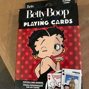 May include: A deck of Betty Boop playing cards. The box is black with the words "Betty Boop PLAYING CARDS" in white. The background is red with white polka dots. The box features an illustration of Betty Boop blowing a kiss. The cards feature custom designs.