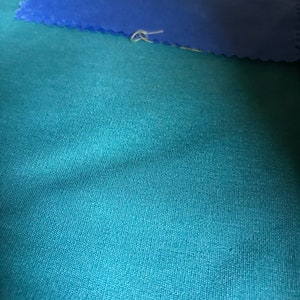 May include: A close-up of a teal fabric with a blue fabric folded on top of it.