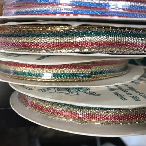 May include: Spools of metallic ribbon in various colors, including red, gold, green, and blue. The ribbon is stacked on white cardboard spools, with the edges of the ribbon visible. The ribbon appears to be for crafting or gift wrapping.