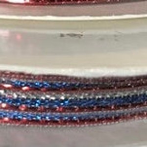 May include: Spools of decorative ribbon in red, white, and blue. The ribbon is spooled on white cardboard discs. The image shows a stack of spools, with the ribbon visible on the edges. The ribbon appears to be glittery.