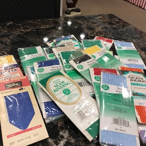 May include: Assortment of colorful woven edge seam binding in various colors, including blue, green, red, and yellow. The packages are labeled with the brand name "COATS" and the text "Woven Edge Seam Binding".