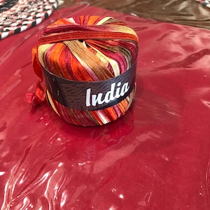 May include: A ball of yarn with a label that says "India". The yarn is a mix of red, orange, and brown colors.