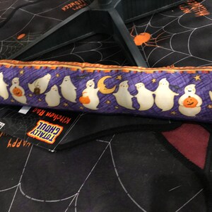 May include: A Halloween-themed kitchen rug with a black background featuring a white spiderweb design and orange spiders. A purple border with white ghosts, pumpkins, and moons decorates the rug. The tag reads "TOTALLY GHOUL Kitchen Rug."