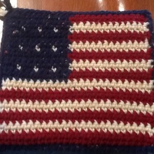May include: A crocheted American flag pot holder in red, white, and blue. The flag is made with a simple stitch pattern and has a blue background with white stars and red and white stripes.