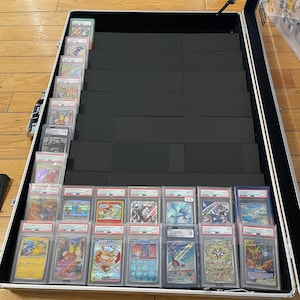 Puede incluir: Maleta negra abierta llena de cartas coleccionables clasificadas. Las cartas están en fundas protectoras transparentes, mostrando ilustraciones coloridas. La maleta está abierta, revelando varias filas de cartas.