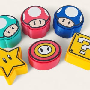 Op de afbeelding: Een verzameling kleurrijke containers en vormen in cartoonstijl. Bevat paddenstoelvormige dozen in rood, blauw en groen, een gele ster, een rood-gele ronde container en een gele doos met een vraagteken.