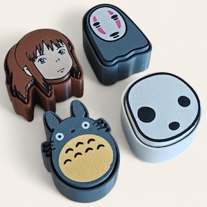 May include: Four character-themed trinket boxes. One box features a girl with brown hair, another a faceless spirit with a white mask, a third a Totoro character, and the last a No-Face character. The boxes are in shades of brown, blue, and white.