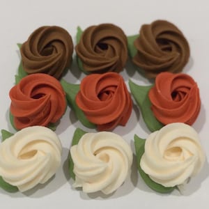 May include: A collection of nine edible-style rose decorations arranged in a three-by-three grid. The top row features three brown roses, the middle row has three orange roses, and the bottom row contains three cream-colored roses, each with green leaves.