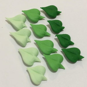 May include: A collection of 12 green leaf-shaped sugar decorations in various shades of green, from light green to dark green.