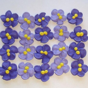 May include: Twenty purple and lavender sugar flowers with yellow centers. The flowers are arranged in a grid pattern.