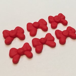 May include: Seven red bows made of fondant or icing. The bows are arranged in a row on a white surface.