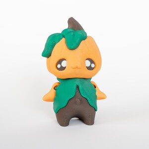 Peut inclure: Figurine fantaisiste d'un personnage à tête de citrouille avec un col en forme de feuilles vertes et des jambes marron. La tête de citrouille est orange avec une tige marron et une feuille verte. Le personnage a de grands yeux expressifs et de petits bras.
