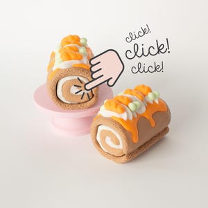May include: A close-up of a miniature pumpkin roll cake with orange frosting and decorative pumpkins. The cake is brown with a white swirl interior. The image includes the text "click! click! click!" and a pointing hand.