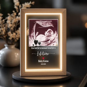May include: A lighted wooden frame displaying a sonogram image of a baby. The frame includes the text "Carried for a moment loved for a Lifetime" with the name "Baby Emma" and the date 01.09.2023.