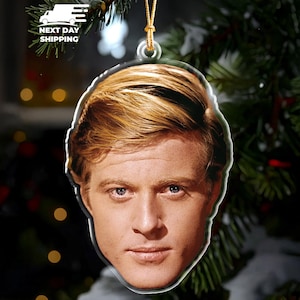 May include: Clear acrylic Christmas ornament featuring a portrait of a man with light brown hair and blue eyes. The ornament is hanging from a gold string against a backdrop of a Christmas tree. The words "NEXT DAY SHIPPING" are visible.