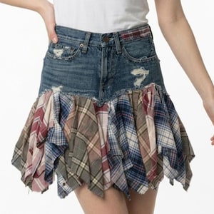 May include: A denim skirt with a patchwork plaid ruffle. The skirt is made of blue denim with distressed details. The ruffle is made of various plaid fabrics in shades of red, blue, and beige. A unique, stylish skirt.